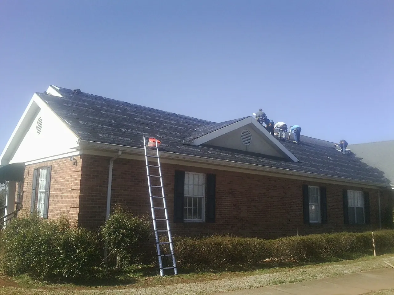 Crew tearing shingles off a brick ranch roof with a ladder set — Emergency Roof Repair work by our crew in San Diego