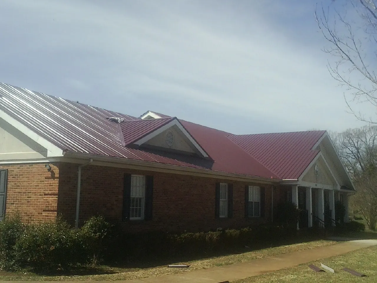 Red metal roof with gabled entries on a long brick building, from a Hail Damage Roof Repair job in San Diego