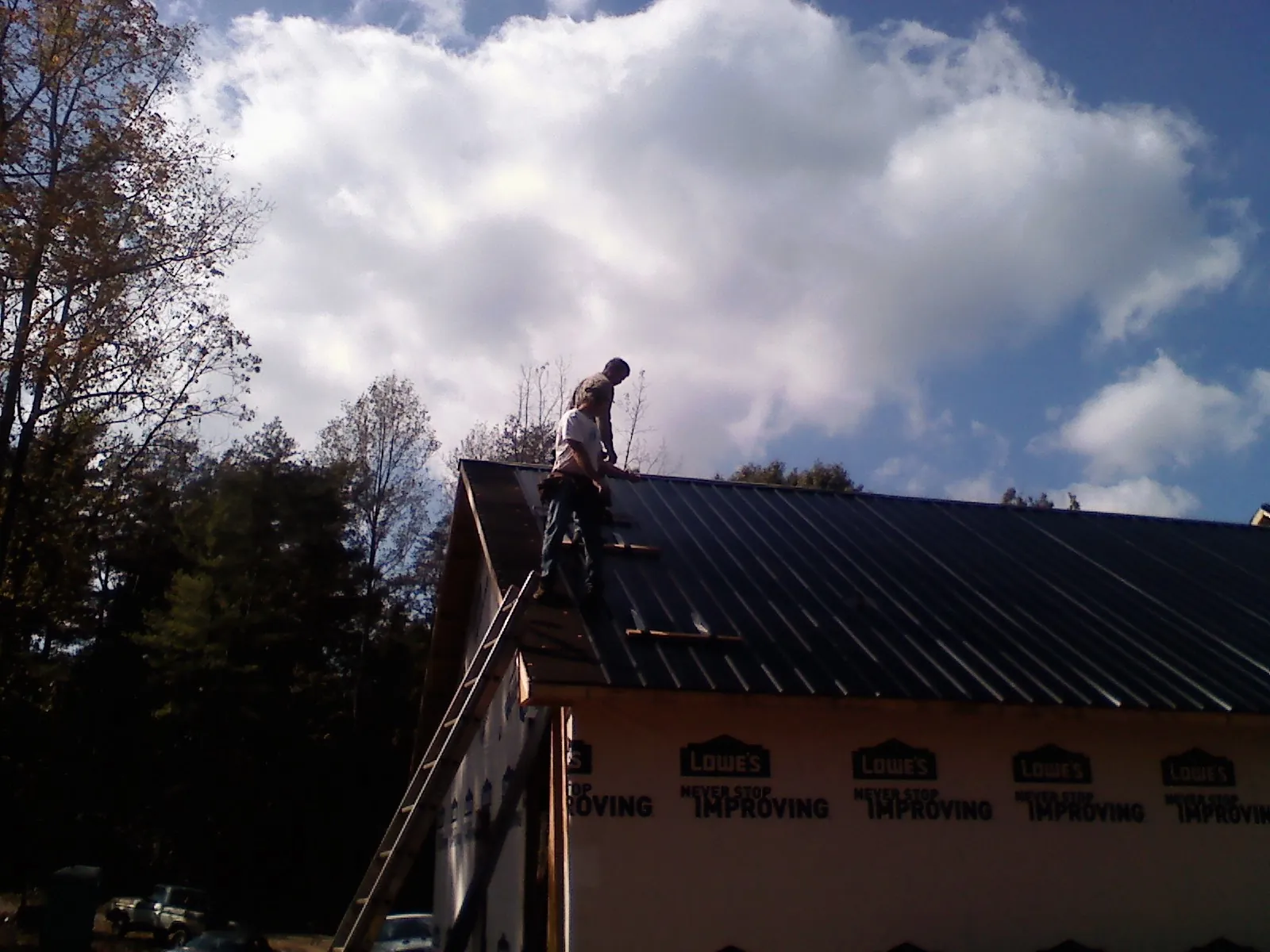 Roofer fastening dark metal panels high against a cloudy sky, from a Roof Inspection job in San Diego