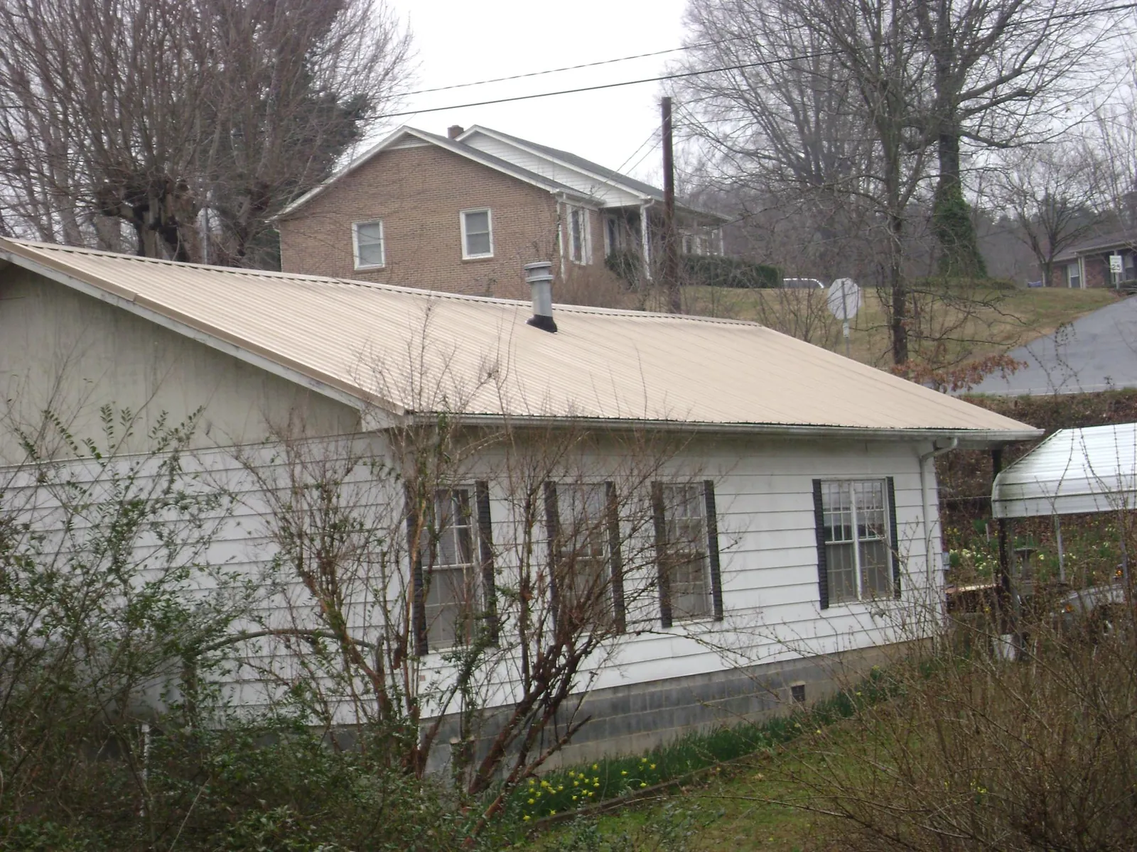 Tan metal roof on a white sided house set into a hillside — Commercial Roofing by Roofing Brothers in San Diego